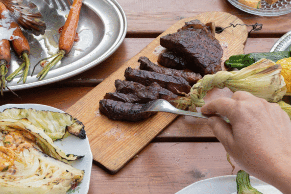 Kesän maut lautasella – grillattua lihaa, maissia ja kasviksia rustiikkisella puupöydällä.