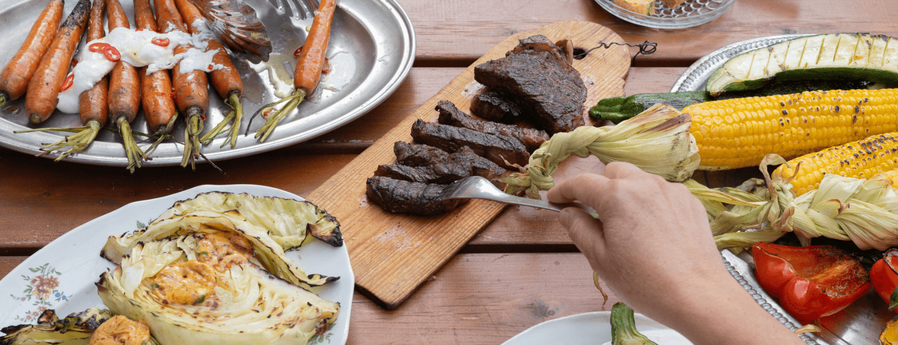 Kesän maut lautasella – grillattua lihaa, maissia ja kasviksia rustiikkisella puupöydällä.